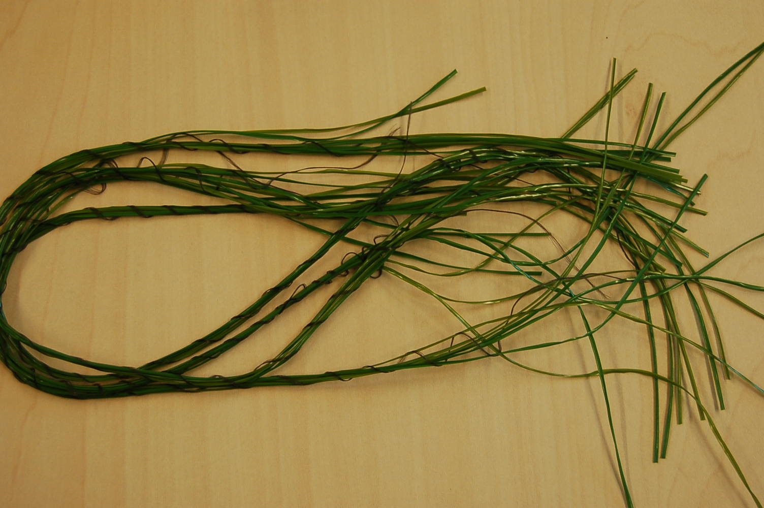 Strippen van synthetische textielstoffen waarvan de schijnbare breedte niet meer dan 5 mm bedraagt.
Het product bestaat uit een bundel van 6 groene strippen die bijeen worden gehouden door 1 zwarte draad.
De strippen hebben een dwarsdoorsnede van minder dan 1 mm en een breedte van ongeveer 1.35 mm (tolerantie 5%).
De groene filamenten zijn vervaardigd van polyethyleen en de zwarte draden van polypropyleen. Het hoogste gewichtspercentage van het samengestelde artikel wordt toegekend aan de strippen van polyethyleen.
De strippen worden –volgens opgave– toegepast voor de vervaardiging van kunstgrasmatten.
