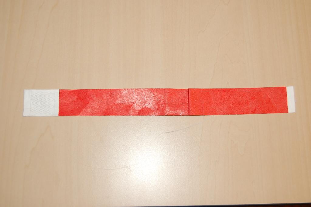 Een polsbandje van gebonden textielvlies met onder andere de volgende kenmerken:
- bestaande uit een strook tyvek;
- van vezels van polyetheen;
- afmetingen van ongeveer 240 x 25 mm;
- waterbestendig;
- een plakstrip aan het uiteinde;
- een sluiting door middel van een plakstrook.
Het bandje wordt gebruikt als toegangsbewijs voor een evenement en kan niet zonder scheuren worden verwijderd.