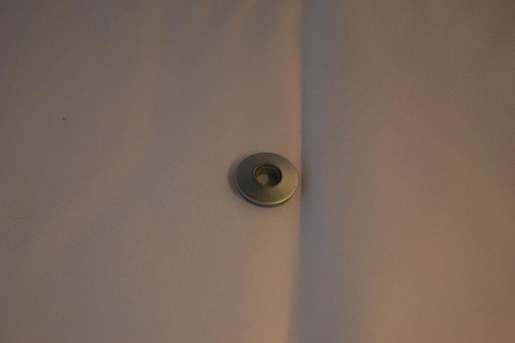 Een samengesteld werk van twee op elkaar geperste ringen met een diameter van ongeveer 1,5 cm en een boorgat van ongeveer 0,5 cm. Vervaardigd van -volgens opgave- een ring van neopreen en een van roestvrij staal. Het wezenlijke karakter wordt toegekend aan de ring van roestvrij staal.