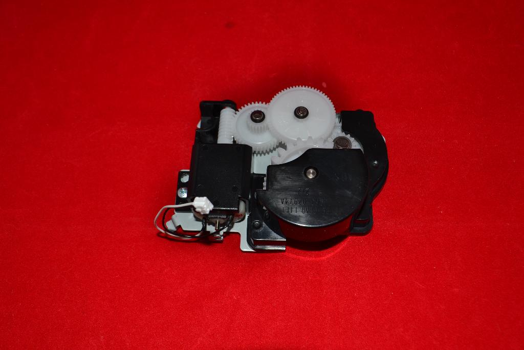 Een zogenoemde printer feed drive, zijnde een tandwielkast, met onder meer de volgende uiterlijke en technische kenmerken:
- een metalen plaat, speciaal gevormd voorzien van bevestigingspunten;
- op de metalen plaat diverse tandwielen, vervaardigd van kunststof, in verschillende maten en inkepingen,
  deels in een behuizing van kunststof;
- een aansluitkabel;
- een –volgens opgave- mechanische motor;
- bestemd voor een bepaald type printer.
Het artikel heeft de functie het papier door te voeren in samenwerking met –volgens opgave- een controller.