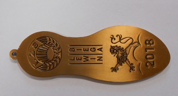 Medal sportowy w kształcie podeszwy buta, wykonany ze stopu cynku, aluminium i miedzi, pokryty farbą emaliową koloru antyczne złoto, nie zawierający kruszców szlachetnych, opatrzony oczkiem do nawleczenia wstążki i posiada wzornictwo sportowe. Medal służy do dekorowania zwycięzców (I, II, II miejsce) za osiągnięcia sportowe i stanowi materialne trofeum, jako dowód zdobycia konkretnej lokaty lub miejsca w zawodach sportowych. Przybliżone wymiary: długość 110 mm, szerokość od 26 mm do 40 mm.