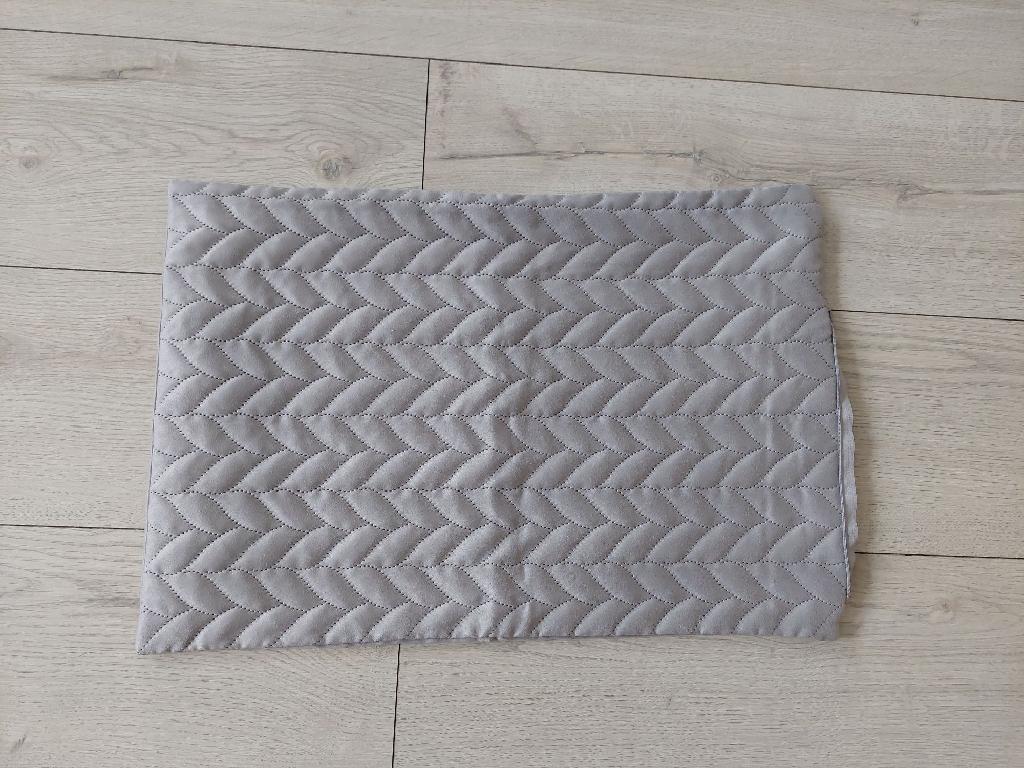Poszewka na poduszkę. Artykuł wykonany z materiału włókienniczego (tkanina 100% poliester) o kształcie prostokątnym (40 x 60 cm), składający się z części przedniej pikowanej oraz części tylnej gładkiej. Dodatkowo przednia część od wewnątrz posiada dodatkową warstwę z włókniny poliestrowej oraz flizeliny polipropylenowej. Przednia i tylna część są połączone ze sobą poprzez zszycie brzegów z trzech stron w czwartym boku jest wszyty zamek błyskawiczny, przez który można włożyć gotową poduszkę. Dostępne różne kolory i wzory pikowania.