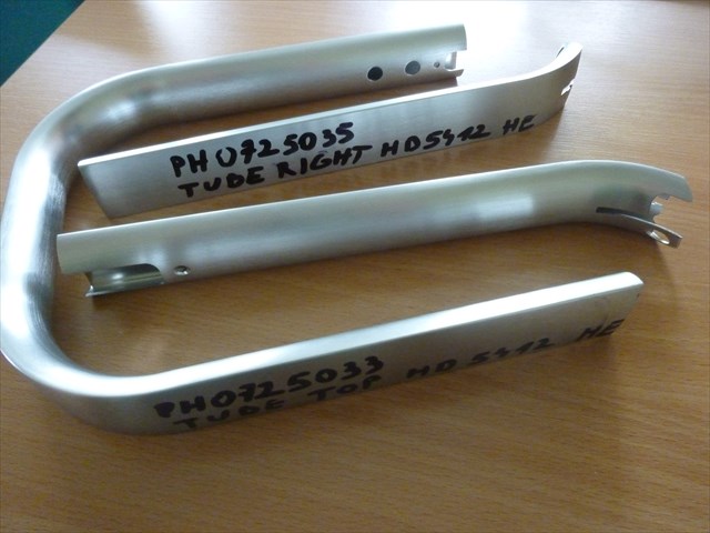 Aluminiowy uchwyt (szkielet), stanowiący część użytkową oraz dekoracyjną przelewowego ekspresu do kawy. Wyrób składa się z trzech części stanowiących całość, które po złożeniu obejmują z zewnątrz ekspres jak i mocują w odpowiedniej pozycji szklane naczynia. Uchwyt wykonany jest z rury o spłaszczonym przekroju poprzecznym o szerokości ok. 36 mm. Górny element w kształcie litery "U" posiada na końcach po dwa otwory. Pozostałe elementy (prawy i lewy) mają jeden koniec lekko wykrzywiony z nacięciami wzdłużnymi. Uchwyty występują w dwóch rodzajach: "LOW END" wykończenie jaśniejsze, "HIGH END" wykończenie ciemniejsze.