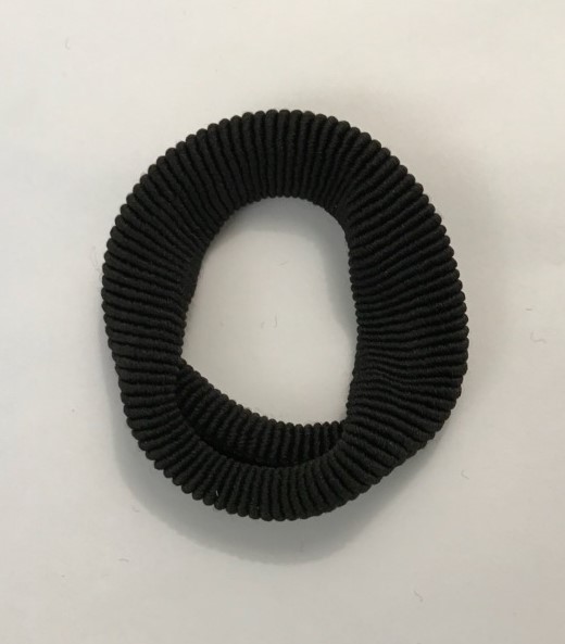 Trikåvara i form av en rundstickad (tubformad), elastisk hårsnodd bestående av syntetfibrer.
Hårsnodden är tillverkad av enfärgad väfttrikå enligt uppgift bestående av 85% polyester och 15% naturlig elastisk gummitråd.
Hårsnodden har i tillplattat skick en längd av ca 8 cm, är skuren till en bredd av ca 4,5 cm och ej vidare bearbetad (inte konfektionerad).