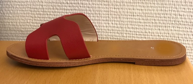 Sko i form av en damtoffel av slip-in modell. Toffeln saknar skaft som täcker ankeln och har låg klack med en höjd av ca 0,5 cm.
Toffeln har överdel och yttersula tillverkade av syntetmaterial enligt uppgift bestående av plast. Överdelen utgörs av en enfärgad rem (med en största bredd av ca 7 cm) över främre delen av toffeln. Remmen är försedd med utskärningar och är fästad vid sulan genom limning.