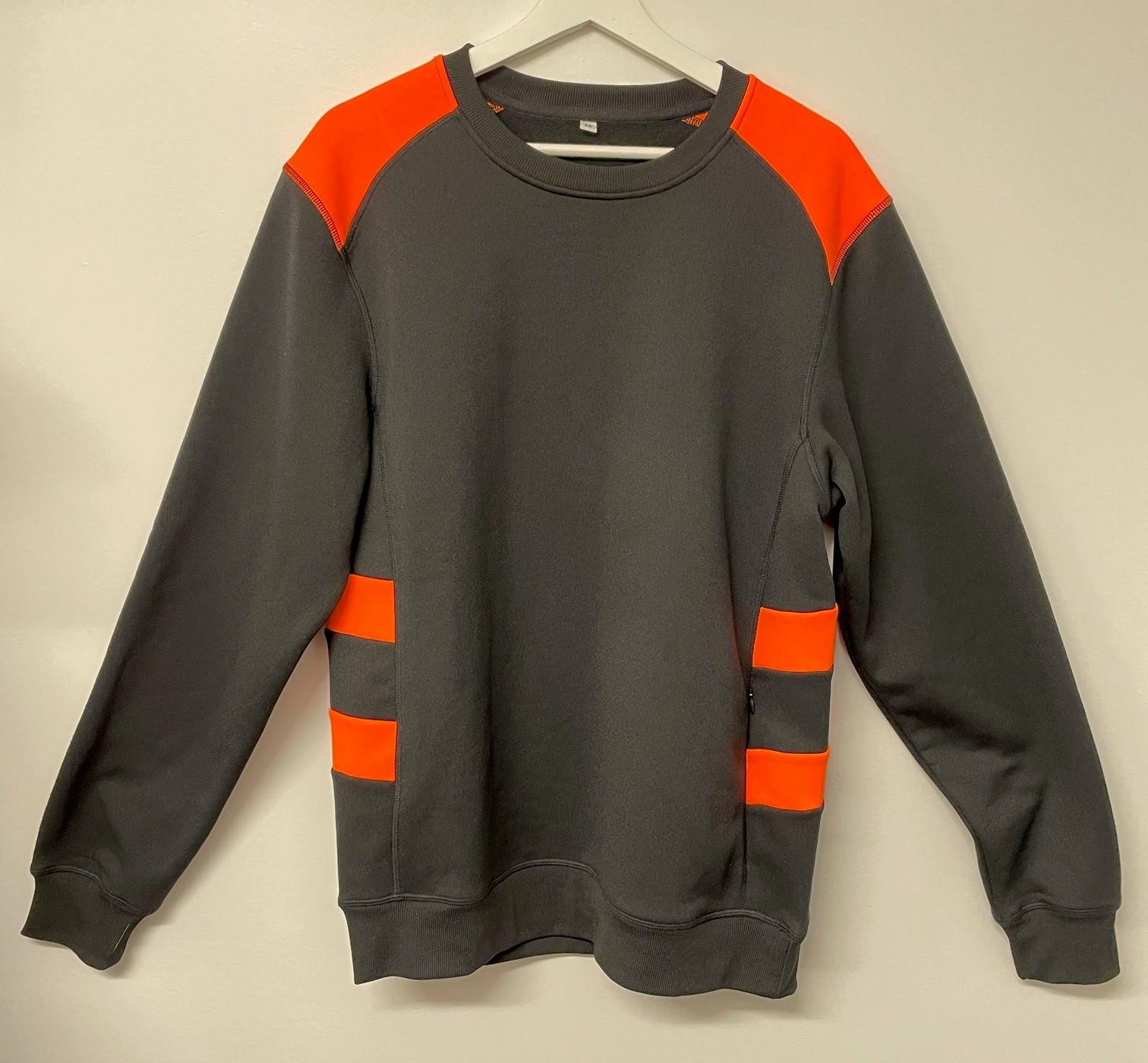 Långärmat ofodrat plagg i form av en tröja (sweatshirt) som är avsedd att täcka överdelen av kroppen ner till strax under midjan. Tröjan har varselfärg på axlarna och sidorna. Tröjan har rund ribbstickad halsringning och en dold sidficka med dragkedja. Tröjan saknar öppning framtill och har ingen tillslutning. Ärmsluten och nederkanten har hopdragningar i form av påsydda ribbstickade muddar.
Tröjan är enligt uppgift tillverkad av dukvara av trikå (100 % polyester) med ruggad insida.
Plagget förekommer enligt uppgift i storlekarna XS - 5XL och är inte igenkännligt vare sig som kläder för män eller pojkar eller som kläder för kvinnor eller flickor och ska därmed klassificeras enligt numret som omfattar kläder för kvinnor eller flickor.