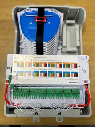 Väggbox av plast, enligt uppgift innehållande en passiv optisk splitter av PLC typ, LC-quad mellanstycken, skarvkassetter, pigtails och slingkorg. PLC-splittern har en ingångsport och 32 utgångsportar och arbetar passivt med optik för att dela en inkommande ljussignal i 32 utgående ljussignaler. Varan är avsedd att användas i ett passivt optiskt nätverk (PON) och innehåller enligt uppgift inga elektriska eller elektroniska komponenter. Varan har måtten 470 x 307 x 147 mm och väger 1,5 kg.