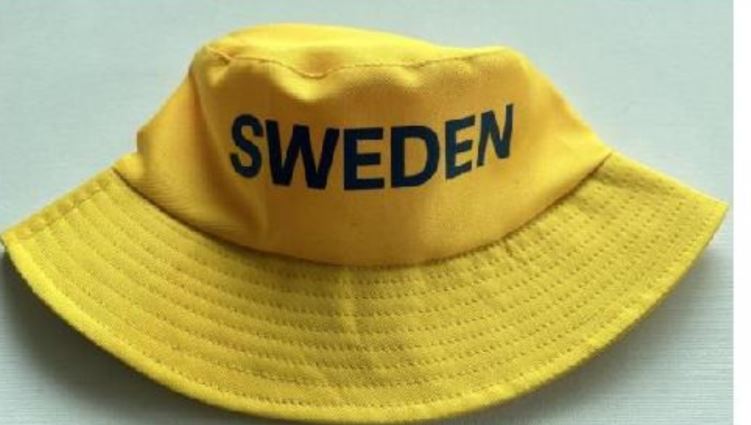 Huvudbonad i form av en gul hatt med blått texttryck och dekorativa sömmar på brättet.

Hatten är enligt uppgift tillverkad av polyesterväv och förekommer i en storlek av unisexmodell.