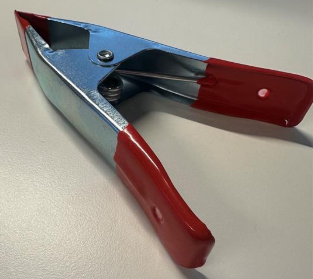 Handverktyg i form av en fjäderbelastad klämma med måtten 15 x 8,5 x 2,5 cm.
Klämman är avsedd att hålla ihop material t.ex. vid limning.
Varan är enligt uppgift tillverkad av rostfritt stål och har ett tunt plastöverdrag på handtag och käftar.
Klämman levereras i detaljhandelsförpackning.
