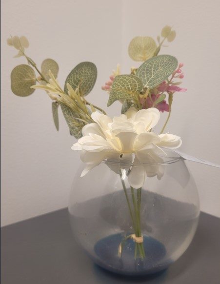 Artikel tillverkad av konstgjorda blommor och blad på kvist i en klotformad vas av genomskinligt glas. Kvistarna är fastsatta i ett blått glasparti i botten av vasen. Varan har en höjd av ca 20 cm.
Avsedd att användas för dekorationsändamål.
Blommorna och bladen är enligt uppgift tillverkade av plast och polyester (textilmaterial). Stjälkarna är av plast. Vasen och det blå partiet, som är fastsatt vasens botten, består av genomsynligt glas.
Blomsterarrangemanget och glasvasen bildar tillsammans en odelbar enhet som inte kan tas isär för separat användning. De konstgjorda blommorna och stjälkarna ger utifrån den dekorativa effekten varan dess huvudsakliga karaktär (regel 3 b) men av de ingående materialen i dessa kan varken plast eller polyester anses vara det dominerande materialet. Därmed ska varan klassificeras enligt det HS-nummer som står sist av de HS-nummer som skäligen kan komma ifråga (regel 3 c).