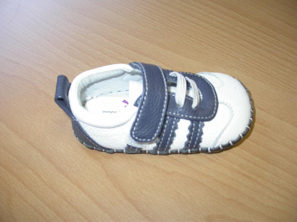 Otroški copati z zunanjim podplatom in zgornjim delom iz usnja. Copati so modre in bele barve, dolžina notranjika je 12 cm, zapenjajo pa se z velcro trakom.