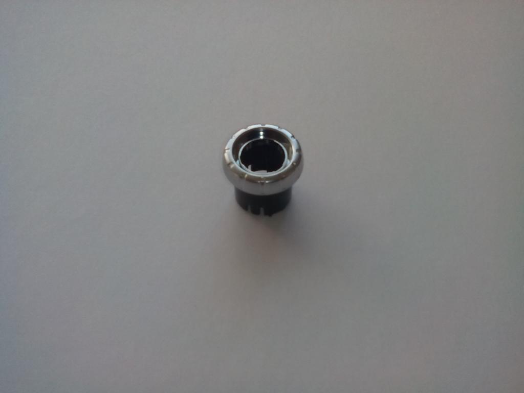 Izdelek je plastični gumb.
Uporablja se kot gumb za nastavitev glasnosti avtoradia na armaturni plošči v avtomobilu.
Narejen je iz akrilonitril-butadien-stirena (ABS) in polikarbonata, prekrit s plastjo bakra (debeline 15 µm), niklja (7 µm) in kroma (0,3 µm). Debelina prevleke je manjša od 49,6 µm.
Gumb je sestavljen iz dveh delov. Spodnji del ima obliko okroglega okvirja premera 24 in dolžine 20 mm. Zgornji del ima obliko prisekanega stožca z osnovno ploskvijo premera 31,5 in višine 7 mm, ki je po celem obodu narebričen.