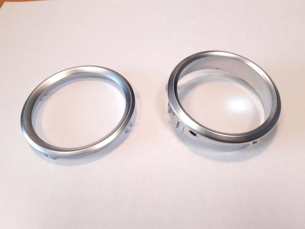 Okvirja iz plastične mase, okrogle oblike:
a)	z zunanjim premerom 92, notranjim premerom 76, višino 12 in okrasnim robom širine 8 mm;
b)	z zunanjim premerom 85, notranjim premerom 70, višino 21 in okrasnim robom širine 7 mm.
Uporabljata se kot okvirja za sprednje plošče za klimatske naprave na armaturni plošči v avtomobilu.
Narejena sta iz akrilonitril-butadien-stirena (ABS) in polikarbonata, prekrita s plastjo bakra (debeline 15 µm), niklja (7 µm) in kroma (0,3 µm).