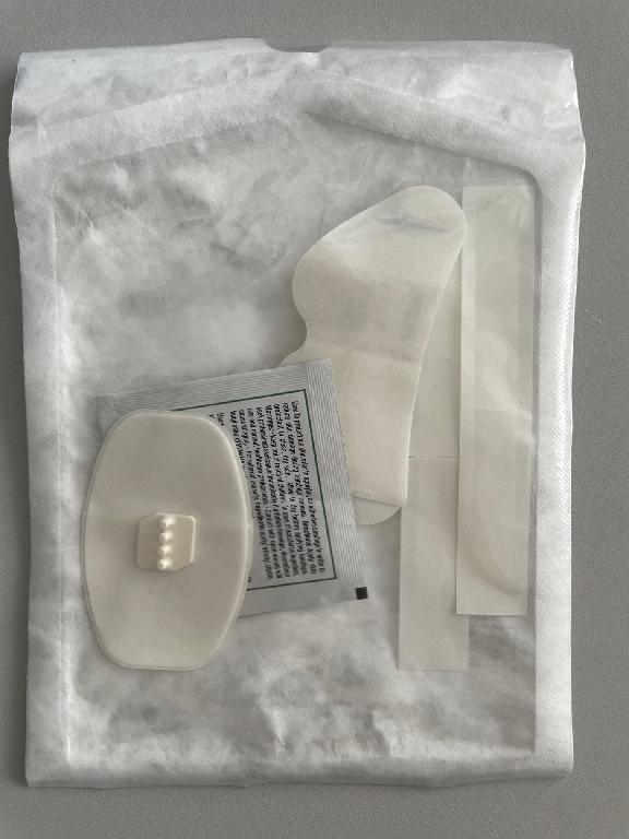 Komplet sestavljen iz:
•	pritrdilnega drsnega dvotočkovnega plastičnega nosilca za kateter pritrjenega na samolepilno podlagi ovalne oblike (velikosti 8 x 4 cm),
•	pritrdilnega štiritočkovnega plastičnega nosilca za cevi katetra na samolepilni spužvasti podlagi ovalne oblike (velikosti 6 x 4 cm),
•	dveh obližev (velikosti 1,6 x 9,5 cm) in
•	robčka prepojenega z acetil-tributil citratom, butil estrom in izopropanolom za pripravo kože pred namestitvijo samolepilne podlage.

Bistveni del kompleta predstavljata nosilca, ki se prepoznata kot pribor katetra.
Namenjen je za medicinsko uporabo, za pritrditev katetra na kožo pacienta.
Komplet je sterilno pakiran v plastično embalažo za prodajo na drobno.